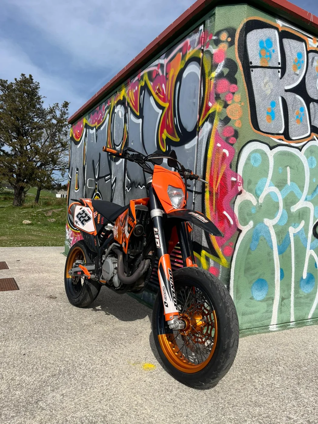 Moto naranja junto a una pared con graffiti como prueba de estilo de vida