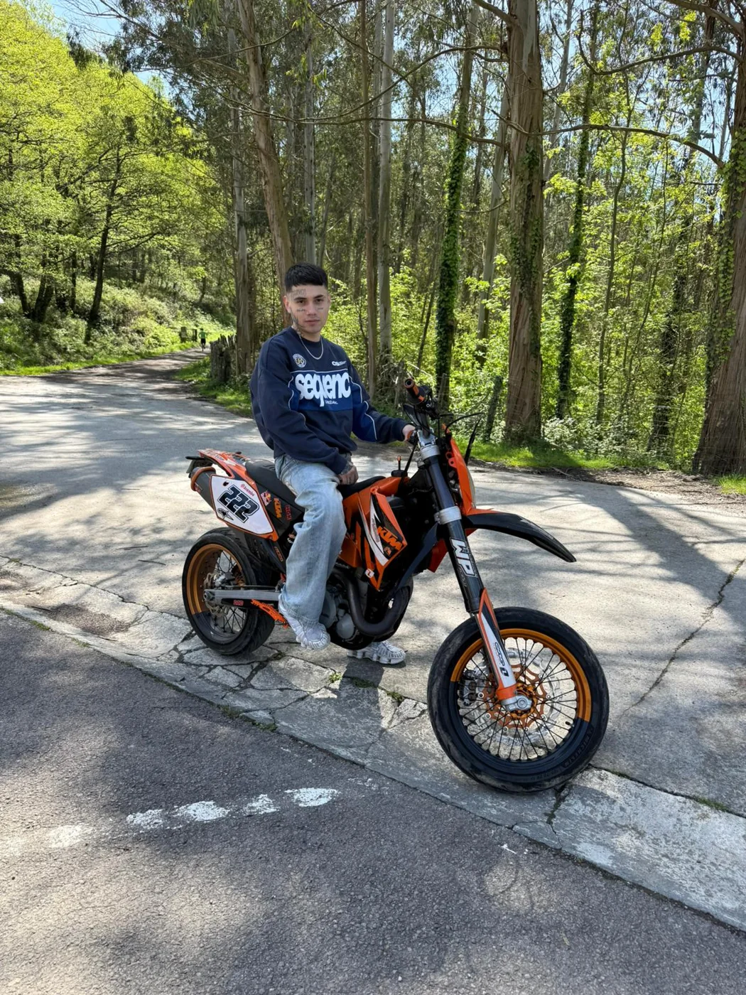 Creador sentado en una moto naranja en una carretera rodeada de árboles